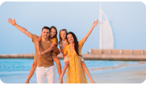 Photo of a family, the mother, father and two daughters in Dubai. They are posing for the photo at the beach, and you can see the Burj Al Arab building in the background.